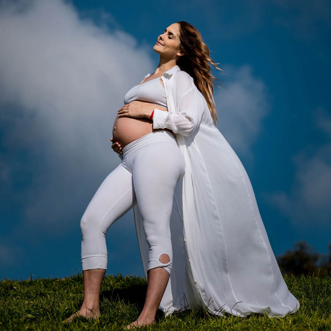 Renowned yoga and meditation instructor Lauren Eckstrom fully pregnant in white clothing with belly exposed, eyes closed and looking up at the sky as part of "initiating the mother," a comprehensive prenatal yoga program